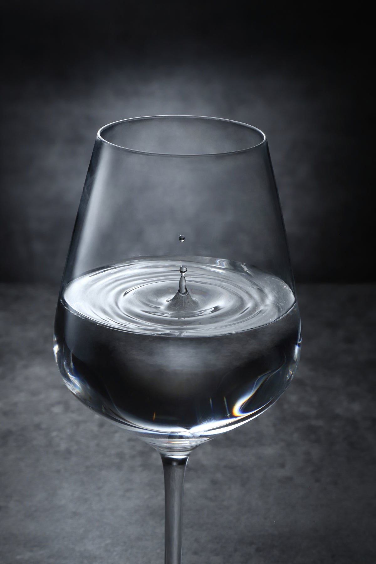 光を受ける日本酒のグラスと、液面に広がる波紋